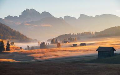 Alpe di Siusi (Seiser Alm) alpine meadow with beautiful foggy sunrise in the background with the Sassolungo and Langkofel mountains and Seceda mountain, South Tyrol - 468111812