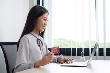 The Asian businesswoman's hand is holding a credit card and using a laptop for online shopping and internet payment in the office