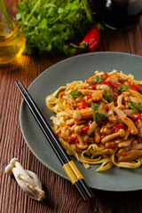 Traditional noodles with shimeji mushrooms and chicken. Prepared in a wok. Served on a gray plate.