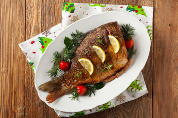 Fried carp whole. Served with lemon and cherry tomatoes on white plate. Christmas decoration. Top...