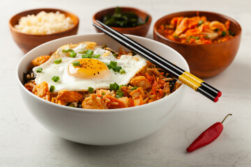 Kimchi cabbage with rice and chicken. Served in a white bowl on a light marble background.