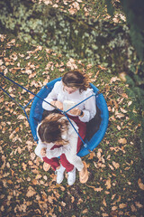 Fototapeta premium two sisters reading a book in a swing in autumn