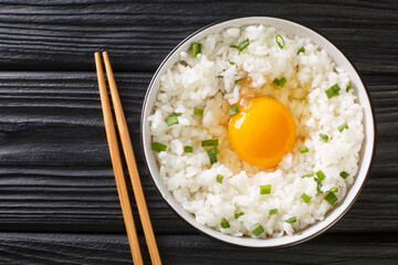 Tamago kake gohan is a simple Japanese dish made of raw Egg Over Rice close up in the bowl on the table. Horizontal top view from above