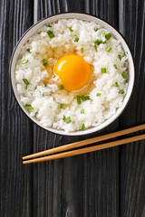 Tamago kake gohan is a popular Japanese breakfast food consisting of cooked Japanese rice topped with raw egg close up in the bowl on the table. Vertical top view from above
