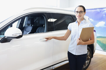 Young woman with documents on hand holding car door in salon