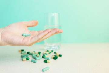 woman's hand holds a pill on green background with glass of water. Pharmacy or health care concept. Copy space