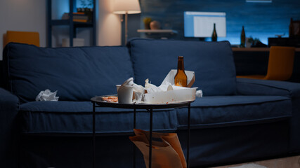 Close up of table with food and booze leftover on misery table in empty unorganized messy living room of depresive person. House apartment of alone woman with sever depresion