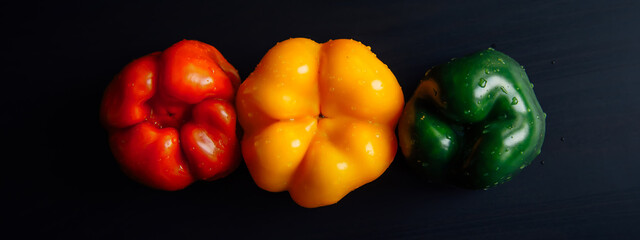 Bulgarian pepper of three colors laid out in a row on black wooden background. Abstract image of traffic light. Concept of healthy eating.