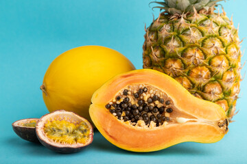 Ripe cut papaya, pineapple, melon, passion fruit, on blue pastel background. Side view, close up.