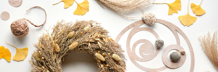 Autumn time background. Dried grass wreath, wood alarm clock, off white table with ginko leaves,...