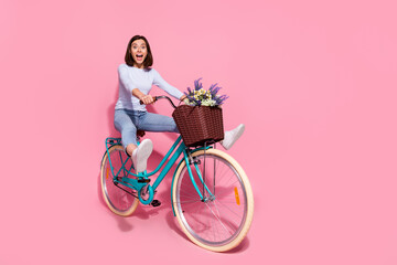 Photo of charming carefree young woman wear white sweater driving bike rising legs empty space smiling isolated pink color background