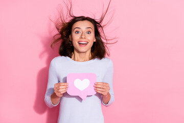 Photo of carefree excited young woman wear white sweater holding notification heart like sign empty space isolated pink color background