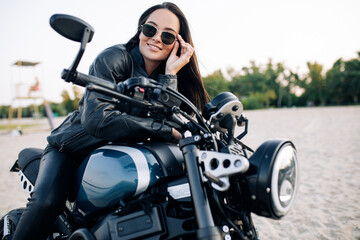 Fototapeta na wymiar Young woman sits on black motorbike among sandy beach.