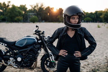 Fototapeta na wymiar Young woman stands in helmet on beach near motorbike.