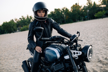 Fototapeta na wymiar Young woman sits on black motorbike in helmet on beach.