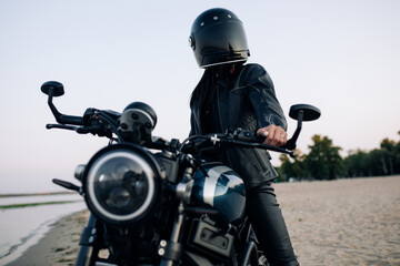 Fototapeta na wymiar Young woman sits on motorbike in helmet on beach near river.