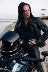 Naklejka na ściany i meble Young woman sits on motorbike on beach next coast of river.