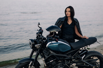 Fototapeta na wymiar Young woman stands next to motorbike on beach near coast of river.