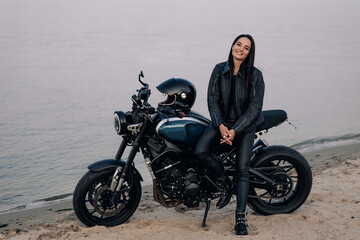 Obraz na płótnie Canvas Young woman stands next to motorbike on beach near coast of river.