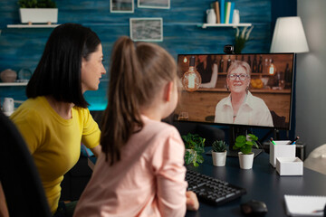 Little child sitting beside parent enjoying discussing with smiling grandmother during online videocall meeting conference. Teleconference call on computer screen. Distance connection