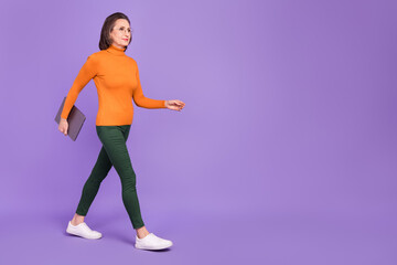 Photo of clever confident lady dressed orange turtleneck glasses holding modern device walking empty space isolated purple color background