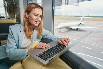 Joyous tourist working on laptop in airport lounge