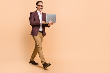 Full length body size view of attractive cheerful man going using laptop copy space isolated over beige color background
