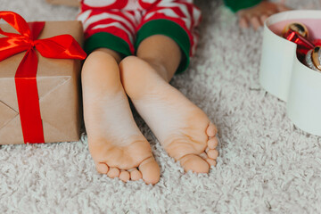 Close-up child's bare feet on his knees near the Christmas tree with Christmas balls. new year...