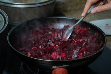 Close-up of a woman's hand mixing beets cut into cubes, carrots, garlic in a frying pan