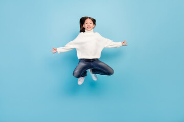 Photo of funny charming student girl wear white sweater smiling jumping high isolated blue color background
