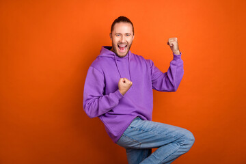 Photo of celebrate young brown tail hairdo guy hands fists yell wear purple hoodie isolated on orange color background