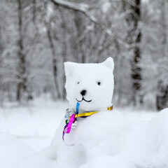 Naklejka na ściany i meble dog made of snow in a multi-colored collar against the background of a winter landscape. cold season for fun