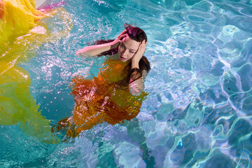 Attractive young woman in yellow dress in water of a swimming pool