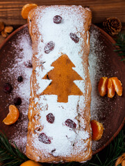 Christmas fruitcake with powdered sugar tangerine cranberry fir tree festive decoration wooden background flat lay. Stollen cake loaf Wholegrain flour dough baking recipe rustic holiday table top view