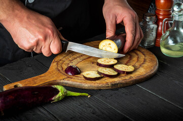 Professional chef is cutting an eggplant in the restaurant kitchen. Close-up of the hands of the cook during work. Delicious breakfast or dinner