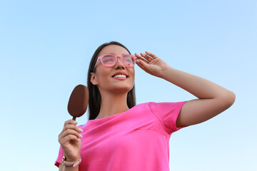 Beautiful young woman holding ice cream glazed in chocolate against blue sky, low angle view
