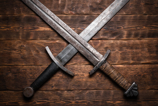 Two crossed swords on the old wooden table flat lay background.