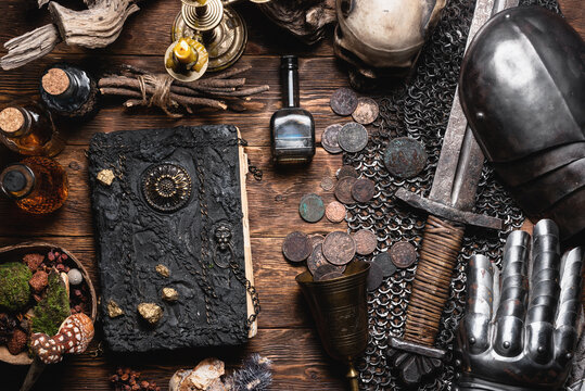 Ancient book and knight sword with an armor on the old wooden flat lay table background. Medieval concept background.