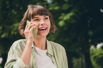 Photo of shiny funny young lady dressed green shirt walking communicating modern gadget smiling outdoors urban park