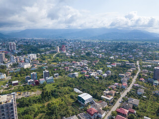 Drone view of private houses and multi-storey buildings against the background of mountains and the sea on a summer day in Batumi.