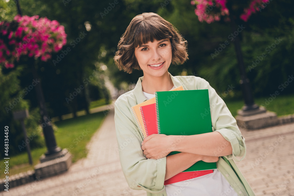 Poster Photo of charming shiny young woman wear green shirt rucksack smiling embracing copybooks walking outside city street