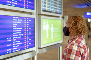 Tourist wearing an FFP2 face mask in front of the flight information boards at an airport. The use of face masks in enclosed areas is now compulsory.