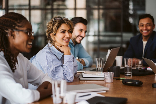 Smiling businesswoman looking away while sitting amidst colleagues at conference table