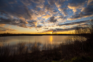 a beautiful blue lake with some tree silhouettes in the foreground under a dramatic sunset sky. High quality photo