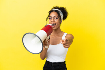 Young african american woman isolated on yellow background shouting through a megaphone to announce...