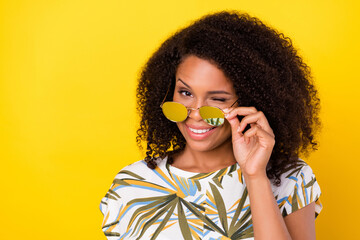 Photo of young pretty afro girl coquettish wink eye hand touch glasses isolated over yellow color background