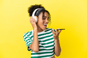Young african american woman isolated on yellow background listening music with a mobile and singing