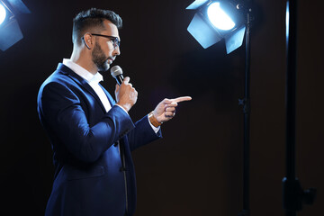 Motivational speaker with microphone performing on stage. Space for text