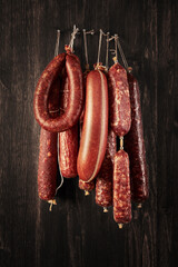 Different types of homemade smoked dry sausages hanging on a dark wooden background. Assortment of...