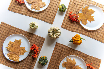 small pumpkins and dry brown maple leafs on white plates, autumn dinner table decors